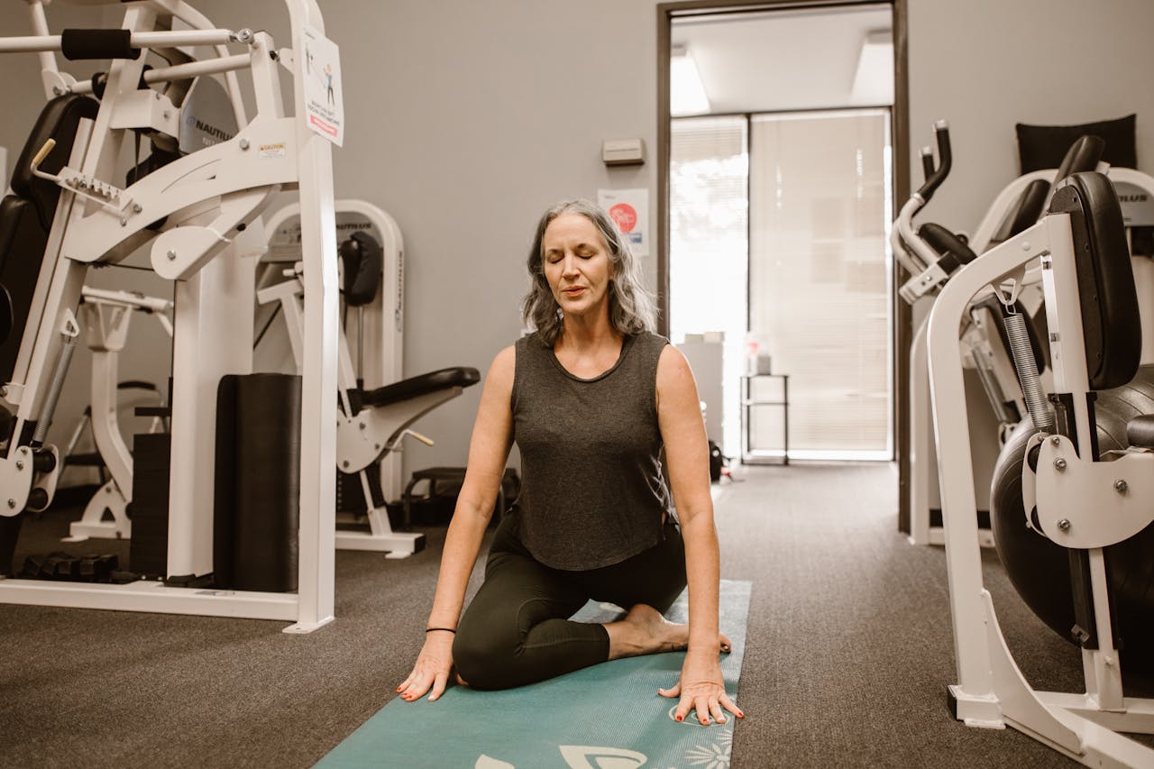 A midlife woman meditates on a yoga mat in a gym, practicing mindfulness and wellness.